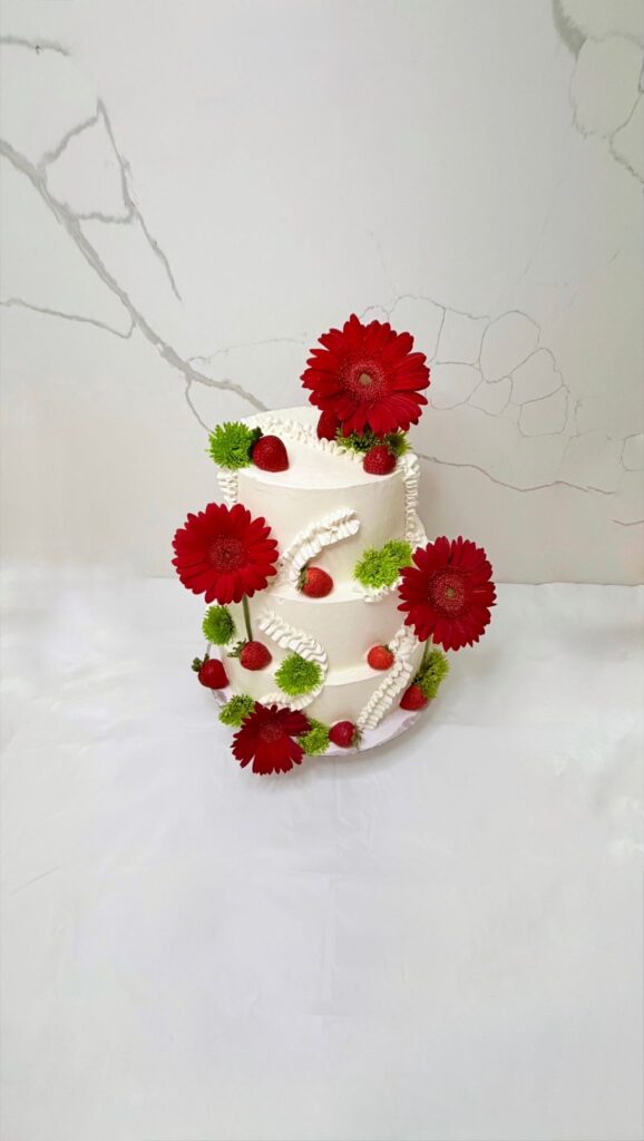 Three-tier white cake with red gerbera daisies and strawberries