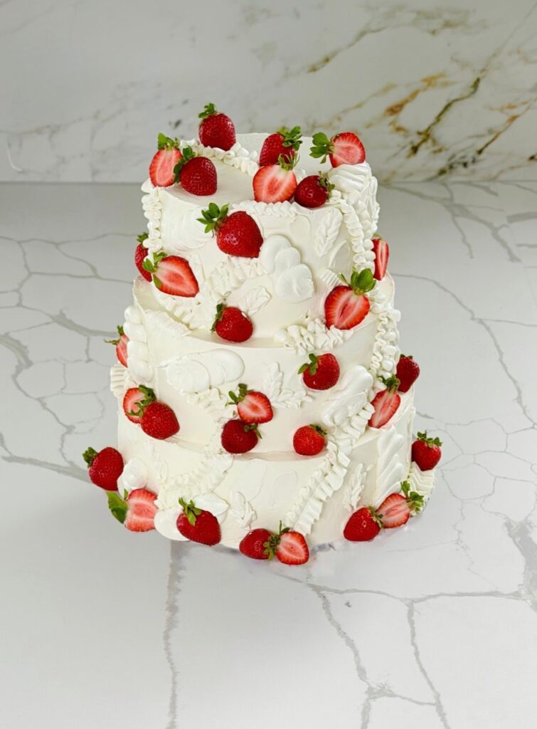 Three-tier white buttercream cake decorated with fresh strawberries